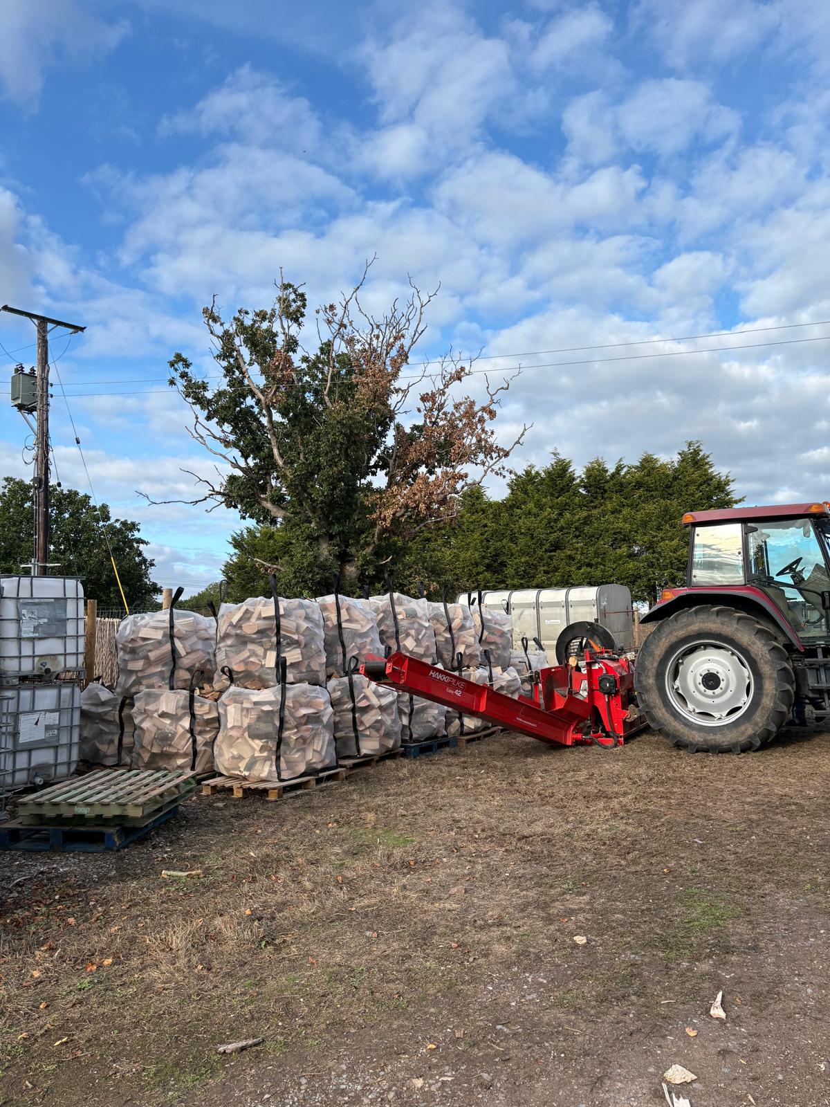 Tractor-powered firewood processor filling netted bulk bags of seasoned logs